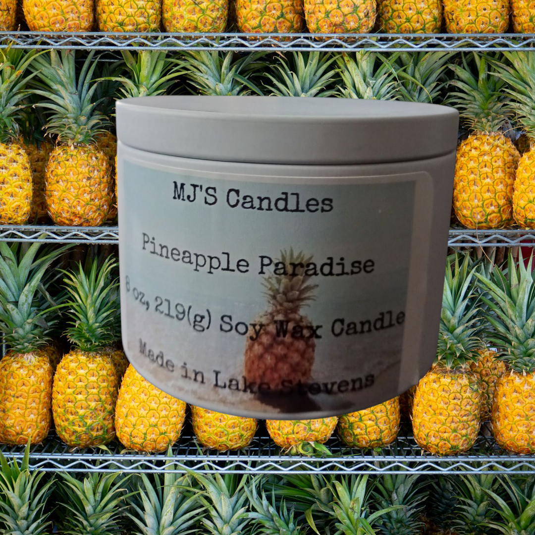 MJ'S Candles handcrafted pineapple paradise candle with soy wax in a gray container displayed against fresh pineapples