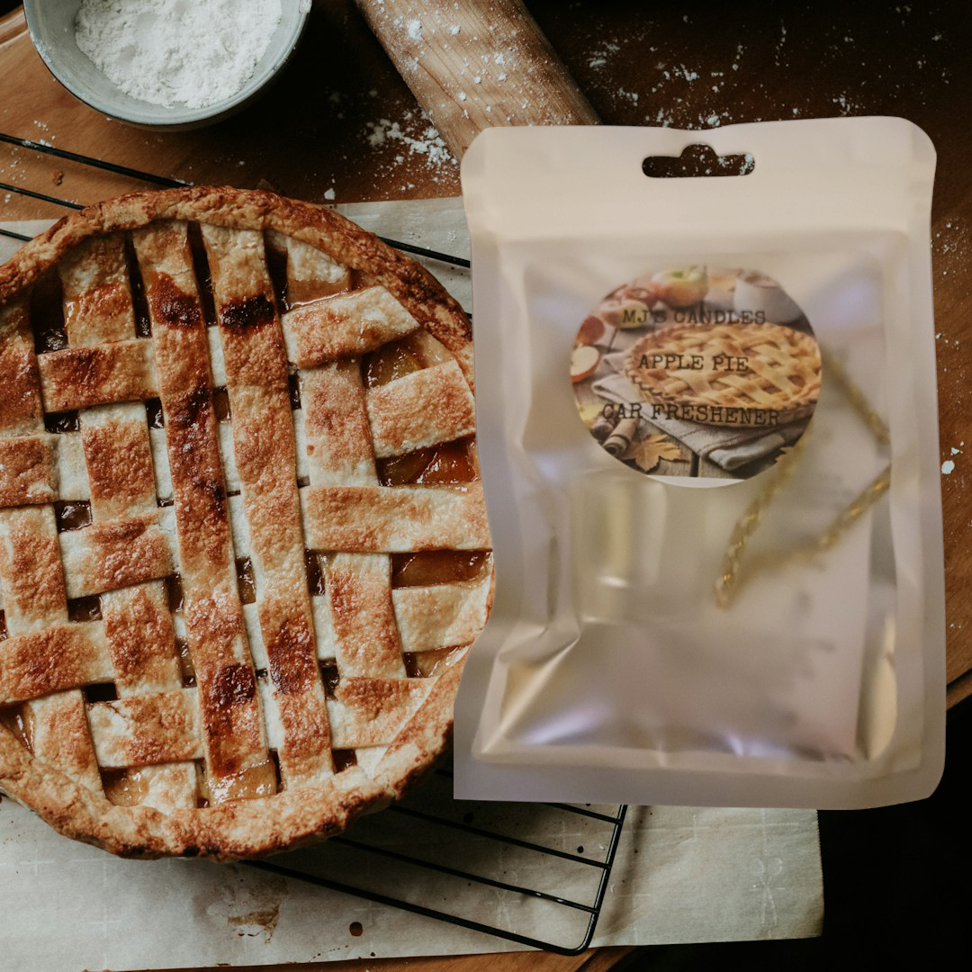 Handcrafted apple pie air freshener packaged next to a freshly baked lattice apple pie on a kitchen countertop