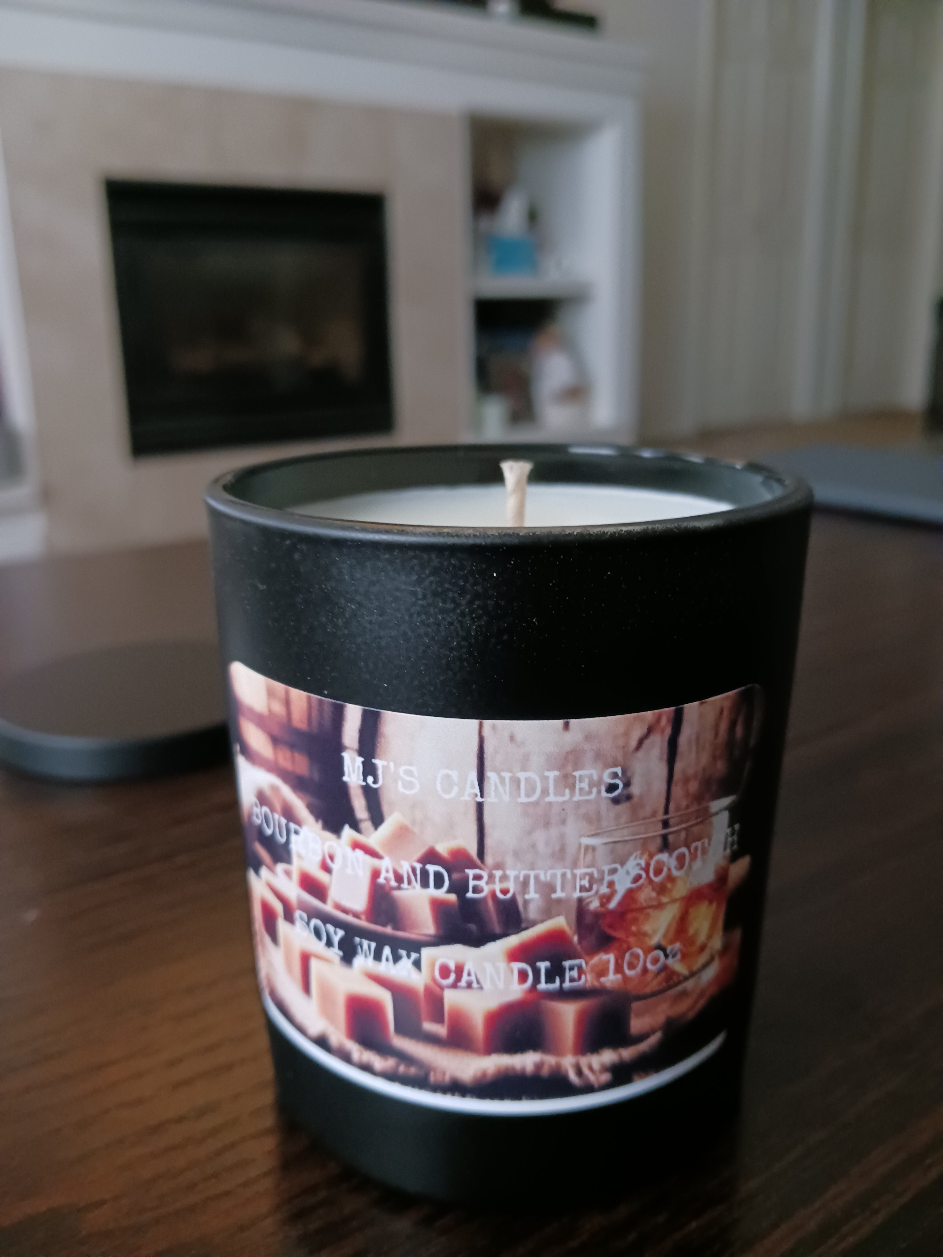 MJ'S CANDLES LLC soy candle wax in a black container with a cotton wick on a wooden table